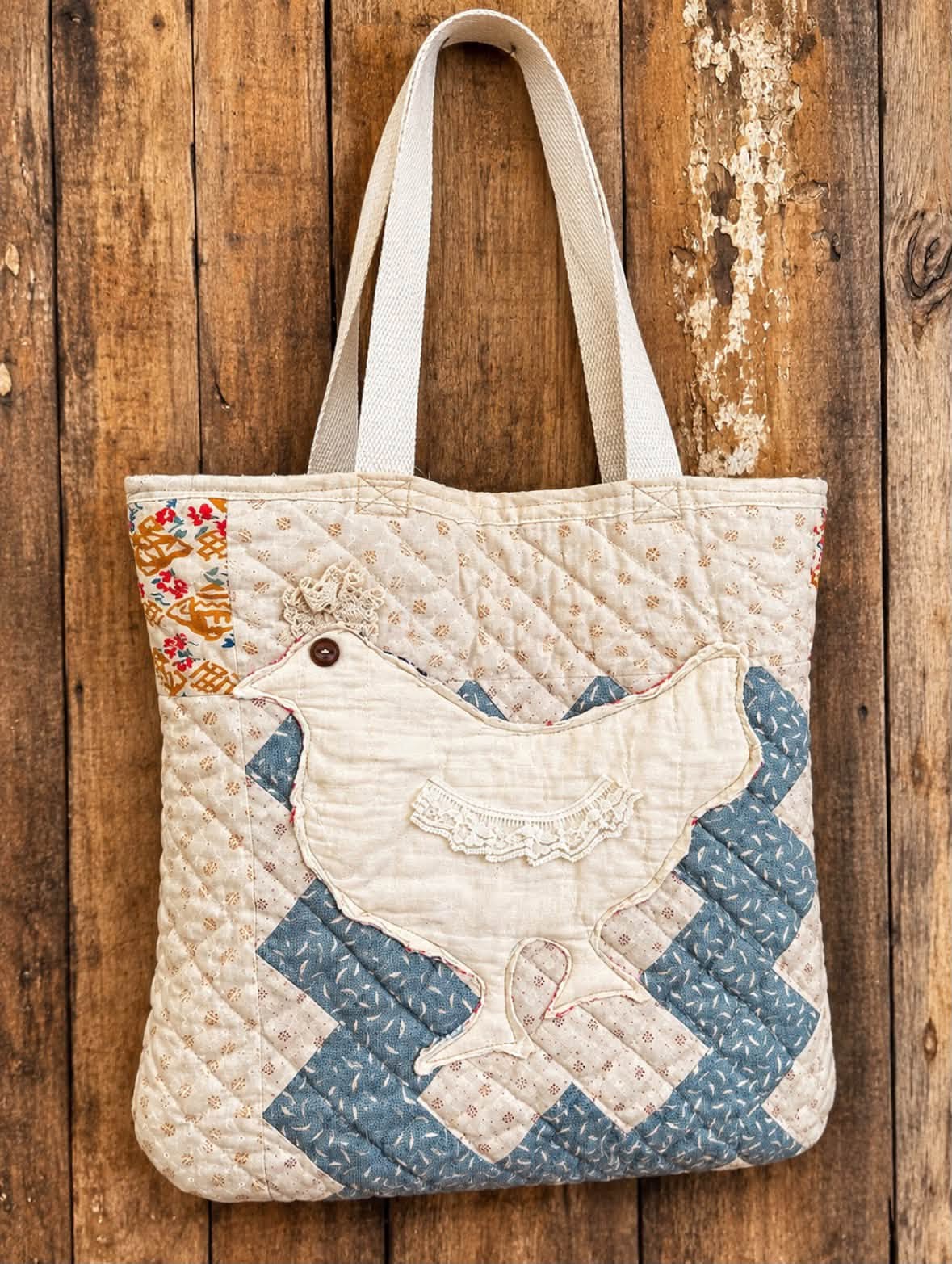 Quilted tote bag with a cream hen appliqué trimmed in ruffled lace and a button eye, set against diamond-quilted cream and slate blue patchwork