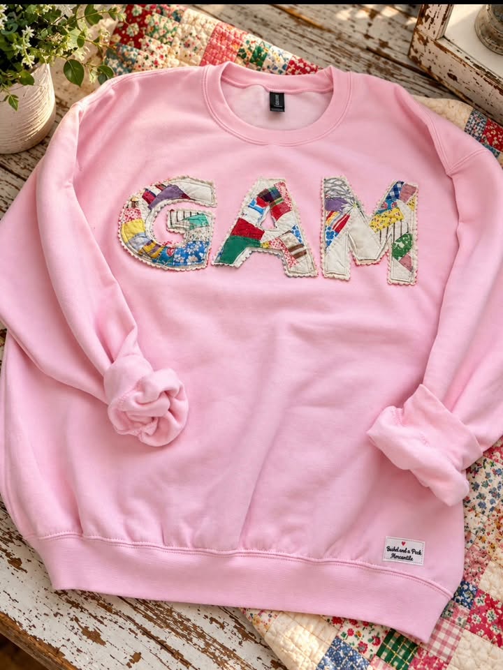 Baby pink sweatshirt with the letters GAM appliquéd from vintage multicolored quilt patchwork and edged with cream scalloped trim