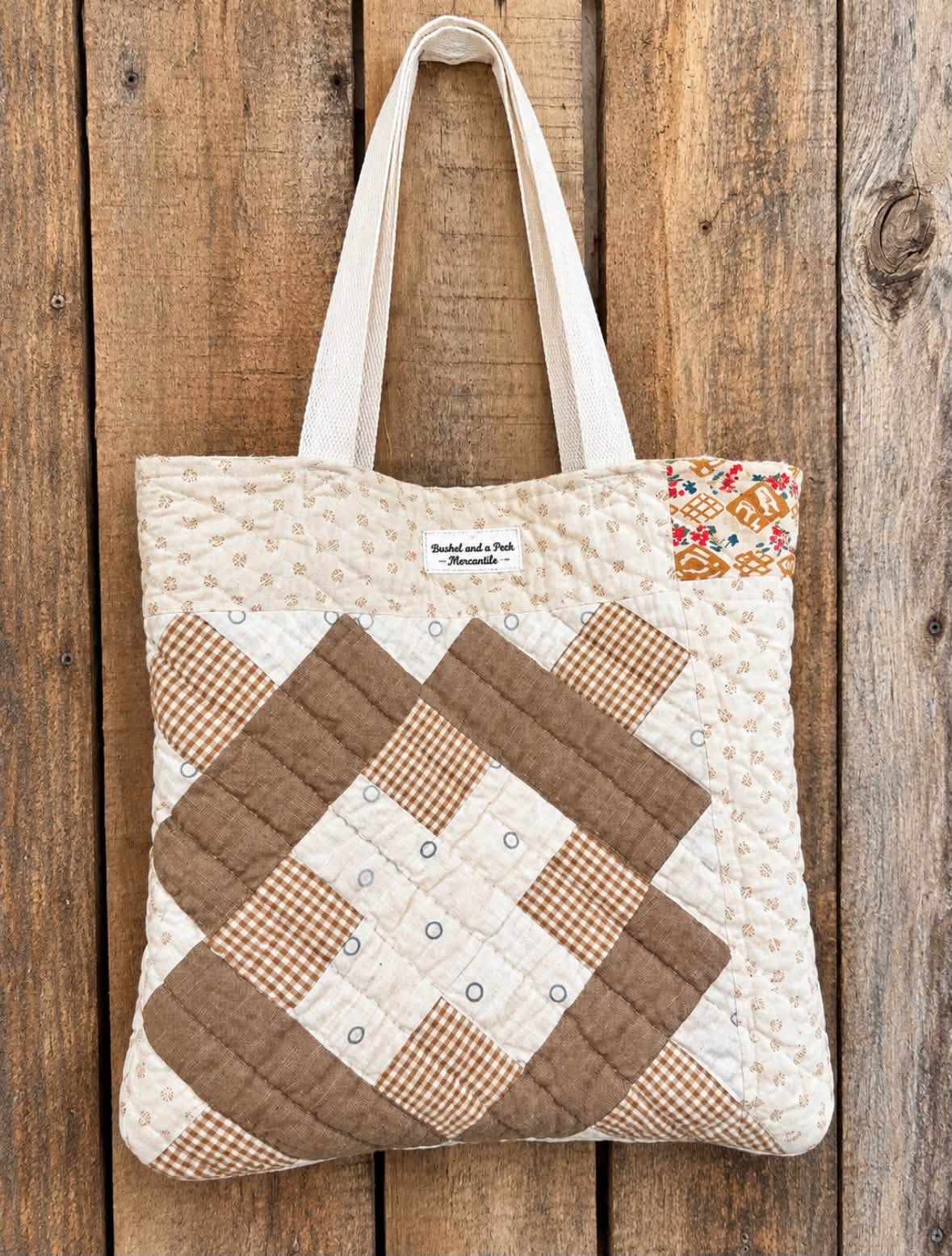 Quilted tote bag with an angled geometric block of brown gingham, warm brown, and cream strips, finished with a Bushel and a Peck Mercantile label