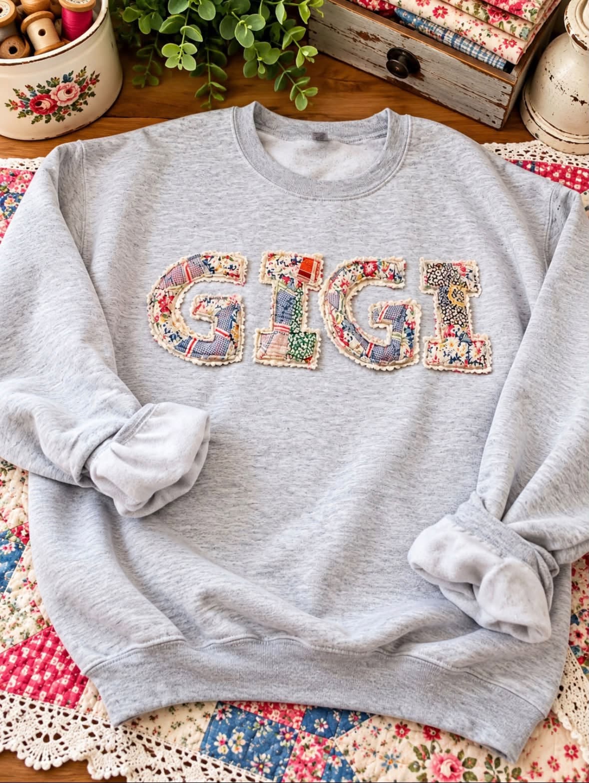 Heather gray sweatshirt with the letters GIGI appliquéd from small pieced quilt squares and edged with cream ruffled trim