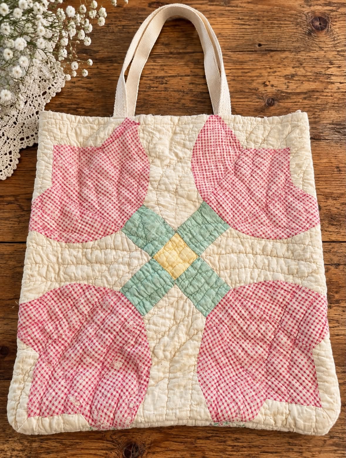 Quilted tote bag made from a vintage tulip quilt block with pink gingham petals around a pale yellow and mint diamond center, laid on a wooden table